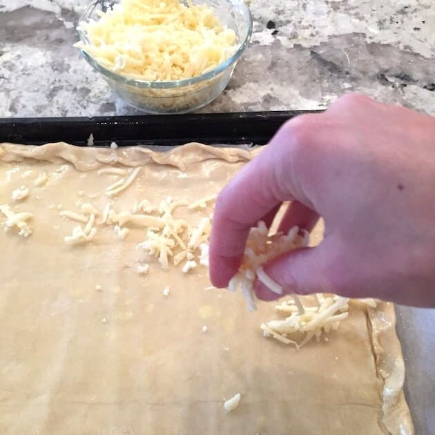 Adding cheese to puff pastry dough with edges crimped