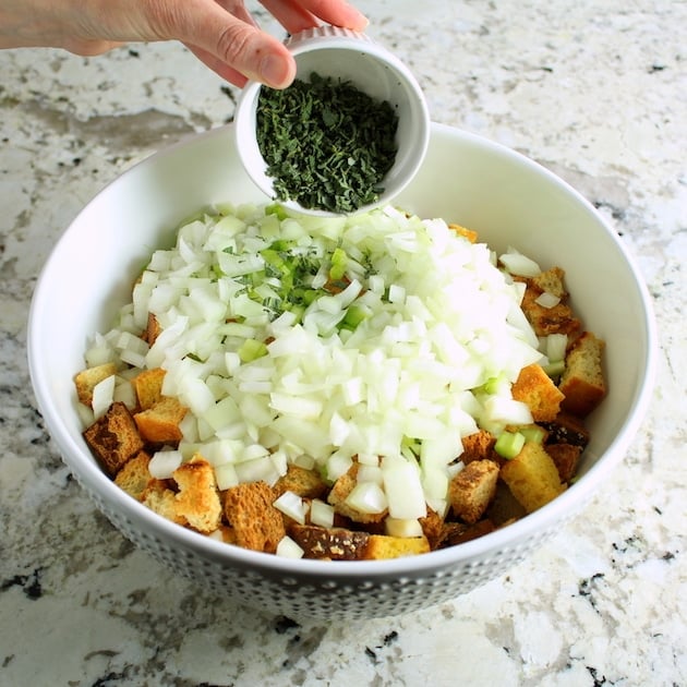 Adding herbs to mixing bowl for turkey stuffing