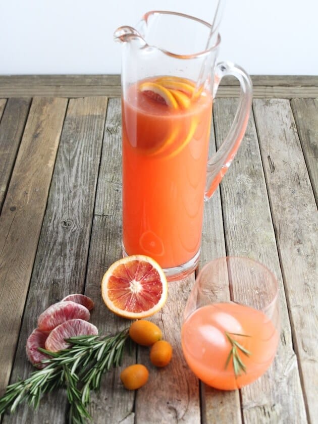 Tall glass pitcher with orange colored punch and fruit