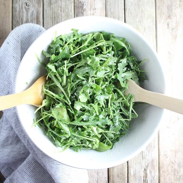 Arugula Salad With Parmesan &amp; Lemon in white bowl with napkin on farm table