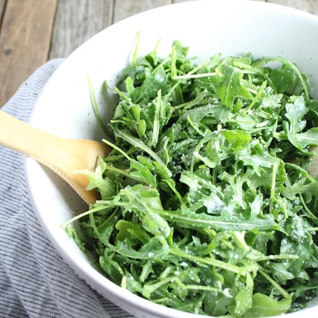 Arugula Salad With Parmesan &amp; Lemon in bowl with wooden spoon on farm table