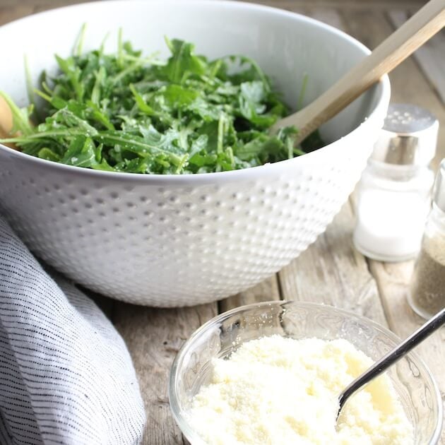 Arugula Salad With Parmesan &amp; Lemon on table with bowl of parmesan and salt shaker