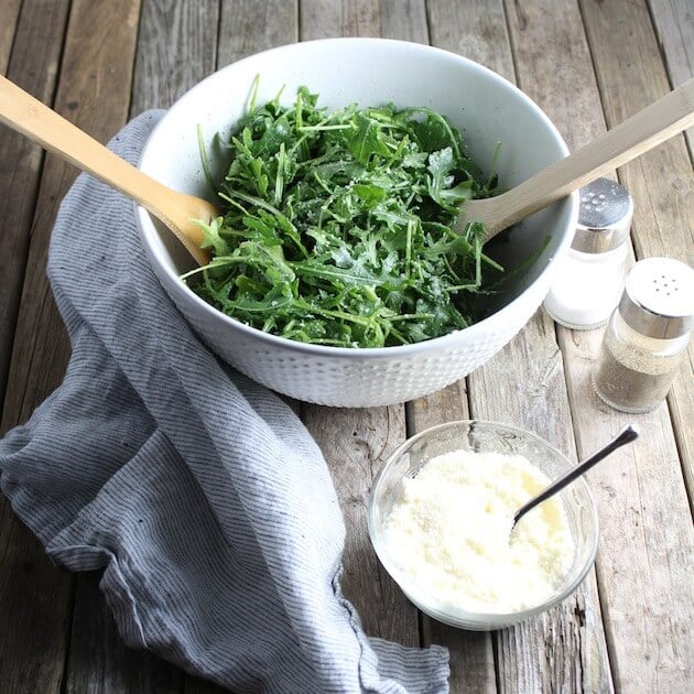 Arugula Salad with parmesan and lemon in white bowl with wooden salad tongs