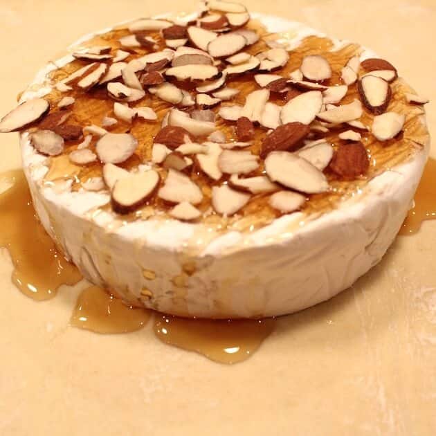 Brie on a sheet of puff pastry with honey and sliced almonds on top.