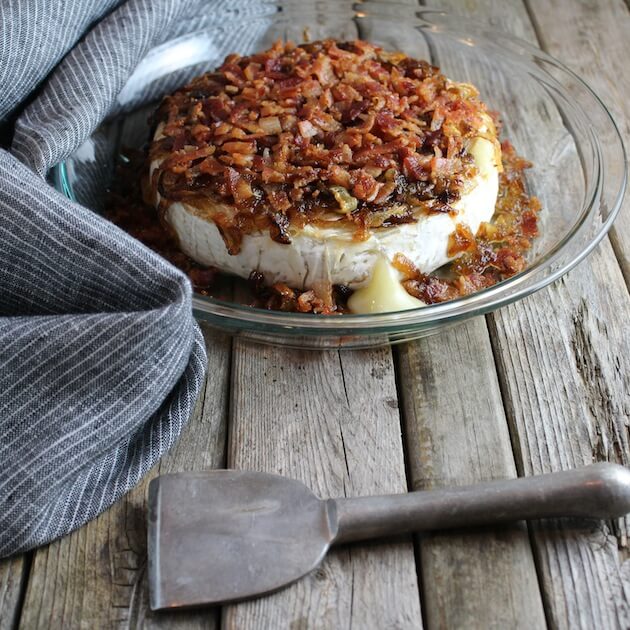Baked Brie in a pie dish on farm table, with Caramelized Onions and Bacon