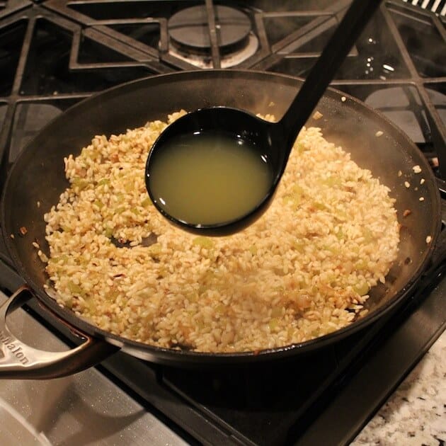 adding ladle of chicken stock to creamy Parmesan Risotto 