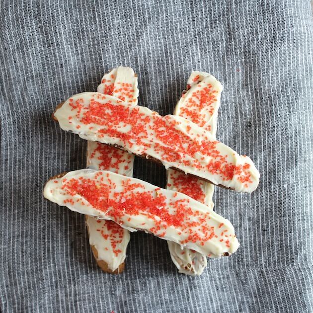 Holiday Biscotti stacked in a hashtag shape, with white frosting &amp; red sprinkles