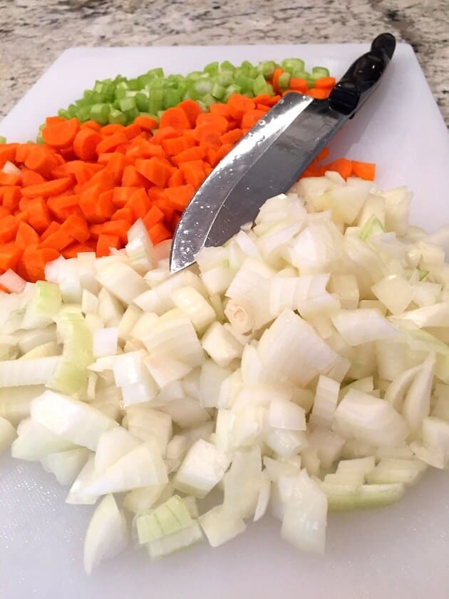Cutting board with chopped onions, carrots, and celery.
