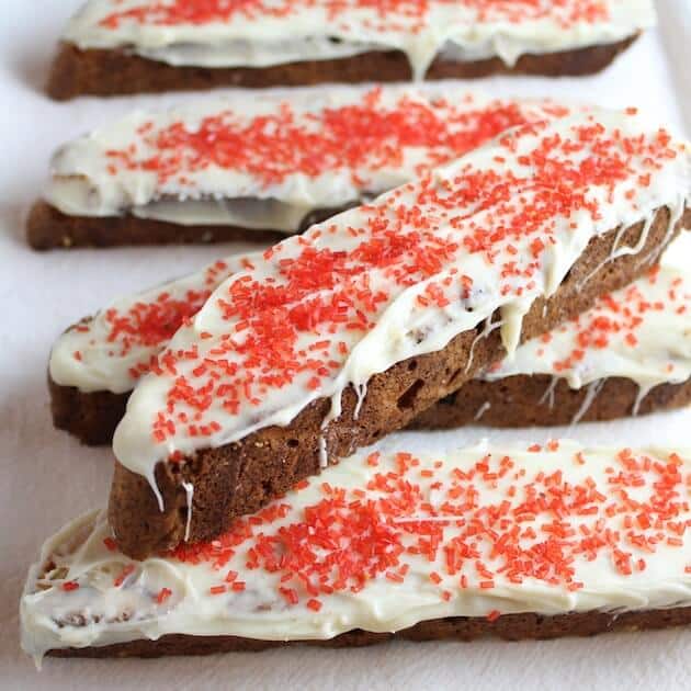 A platter with holiday biscotti with white frosting and red sprinkles.