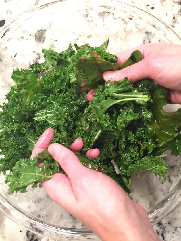 Massaging kale in a glass bowl with olive oil