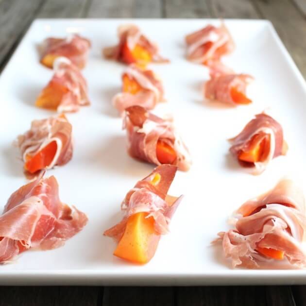 Persimmon slices wrapped in prosciutto on platter