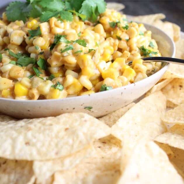 Creamy Cheesy Corn Dip in a bowl surrounded by Corn Chips