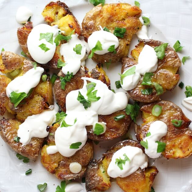 Flattened cooked baby potatoes with sour cream, parsley, and green onions