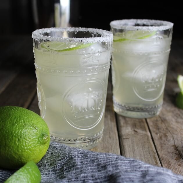 Two margaritas with salted rims and lime garnish