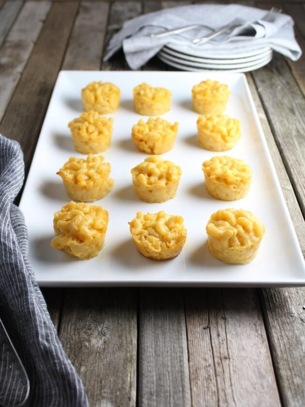 Macaroni and Cheese mini appetizers on farm table with stack of plates