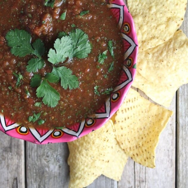 partial bowl of red mexican salsa with corn chips on the side