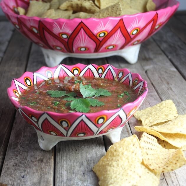 Salsa on a farm table with bowl of chips in the background