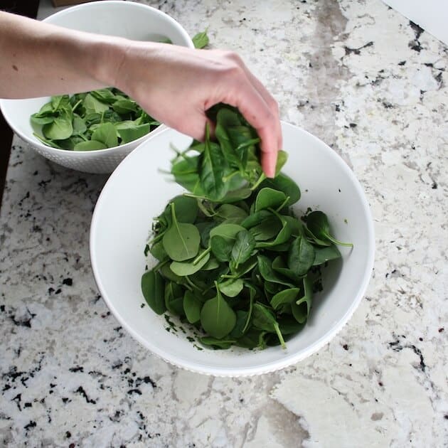 Adding fresh spinach to white mixing bowl for spinach cauliflower salad