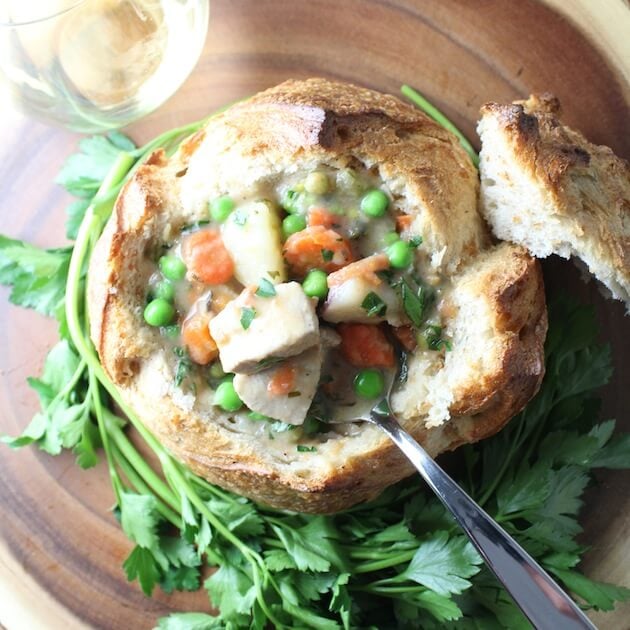 Chicken Soup in a bread bowl with parsley garnish and a glass of wine