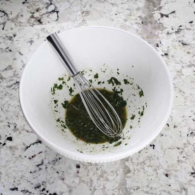 Wire whisk with salad dressing in white salad bowl