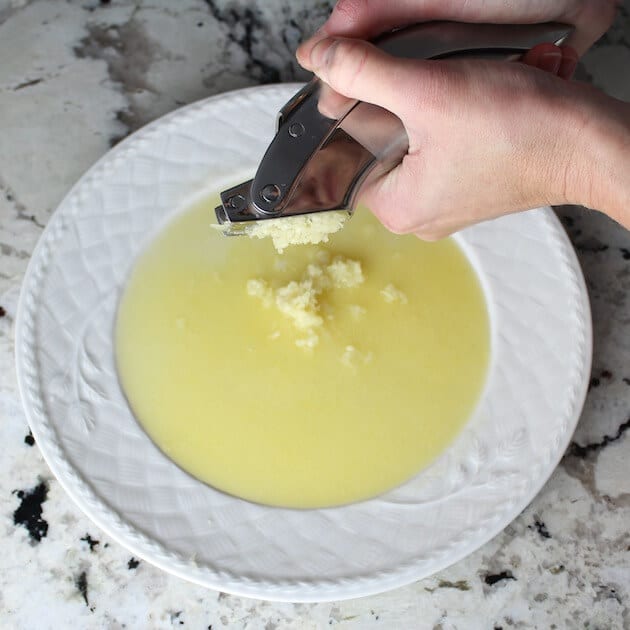 Mincing garlic onto plate with melted butter and lemon