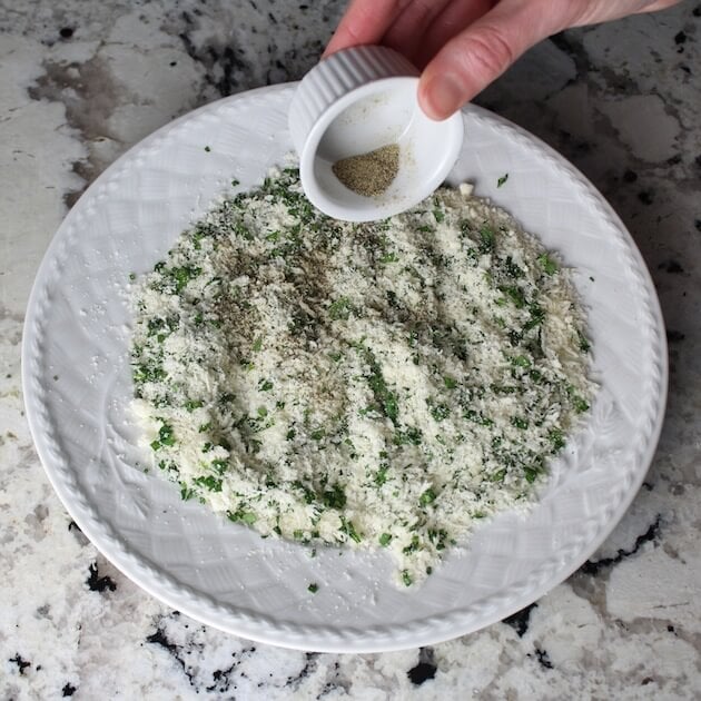 Adding pepper to plate of cheese and herbs