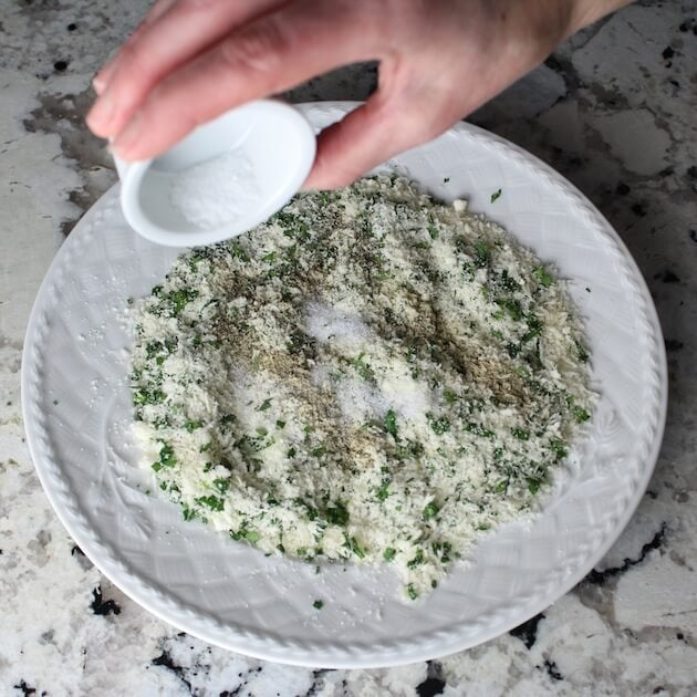 Adding salt to plate of parmesan and herbs