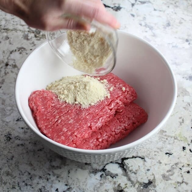 Adding Almond meal to ground beef in the mixing bowl.