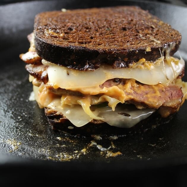 Eye -level view of layers of kimchi Reuben sandwich cooking in cast iron skillet.