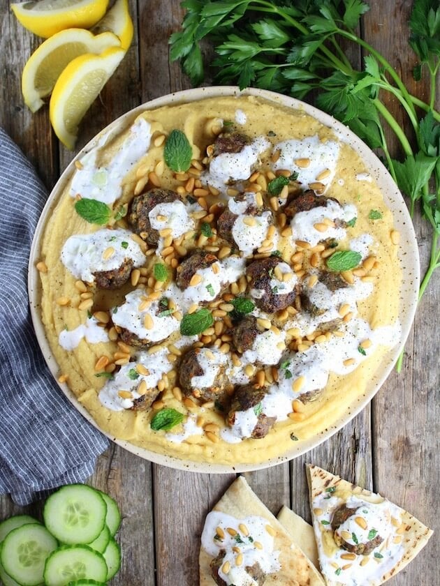 Lamb Meatballs on a platter garnished with mint, beside cucumbers and pita