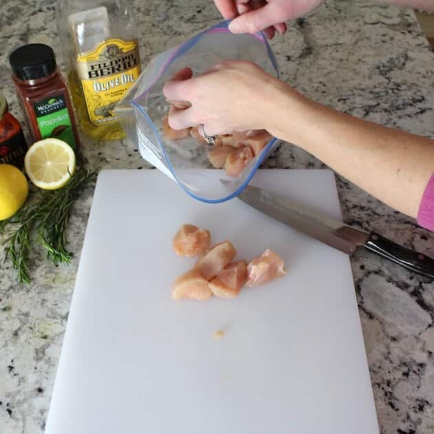 Putting cut up raw chicken into plastic ziploc bag for marinating