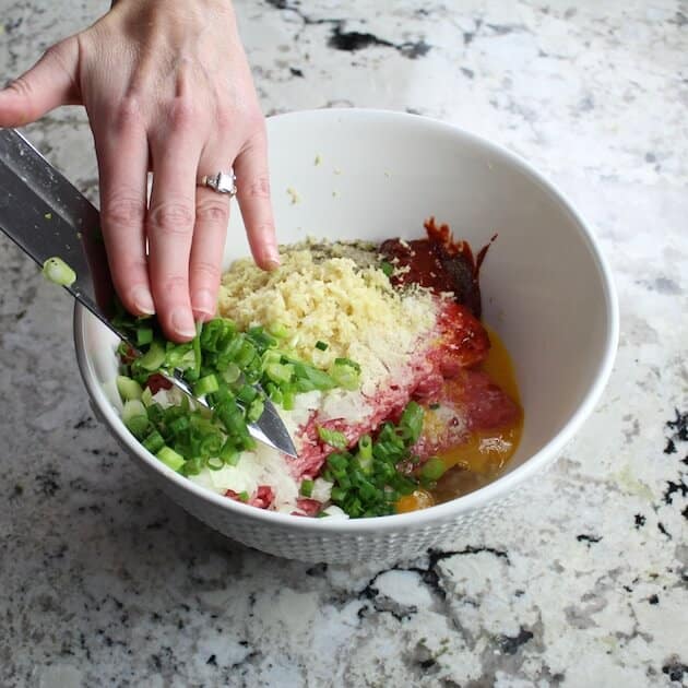 Adding green onions to bowl of meatball ingredients