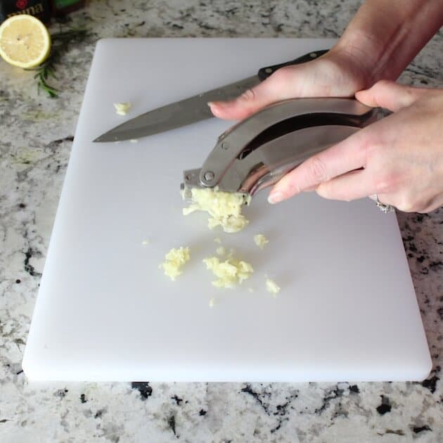 Mincing garlic onto a cutting board.