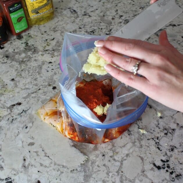Adding garlic to resealable back with chicken and harissa marinade