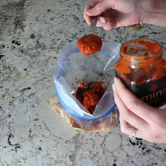 Adding Harissa sauce to resealable bag for marinating chicken.