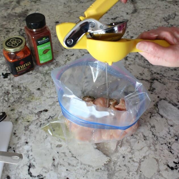 Juicing lemon into resealable bag to marinate lemon harissa chicken