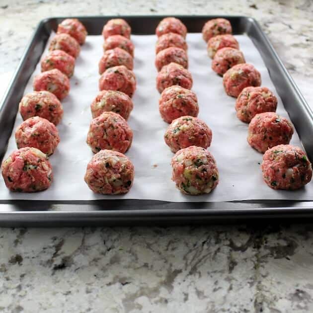 Meatballs linked up on baking sheet with parchment paper ready to cook 