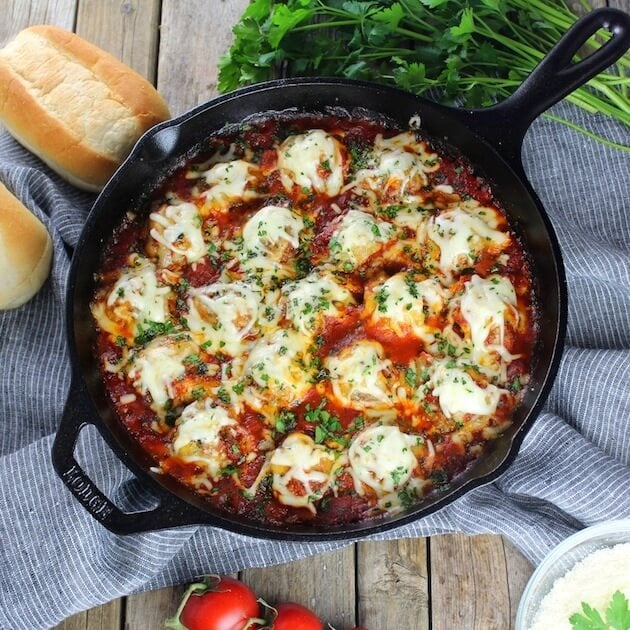 Skillet full of Italian meatballs in red sauce covered with cheese