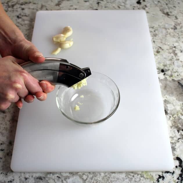 Mincing garlic into a glass bowl on cutting board