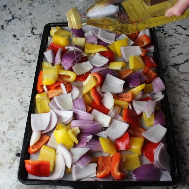 Adding olive oil to veggies on a baking sheet.