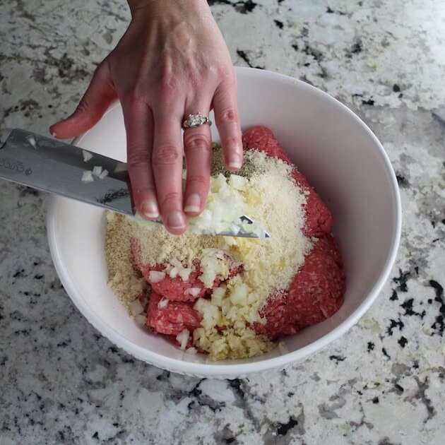 Adding the onion to mixing bowl of meatball ingredients.