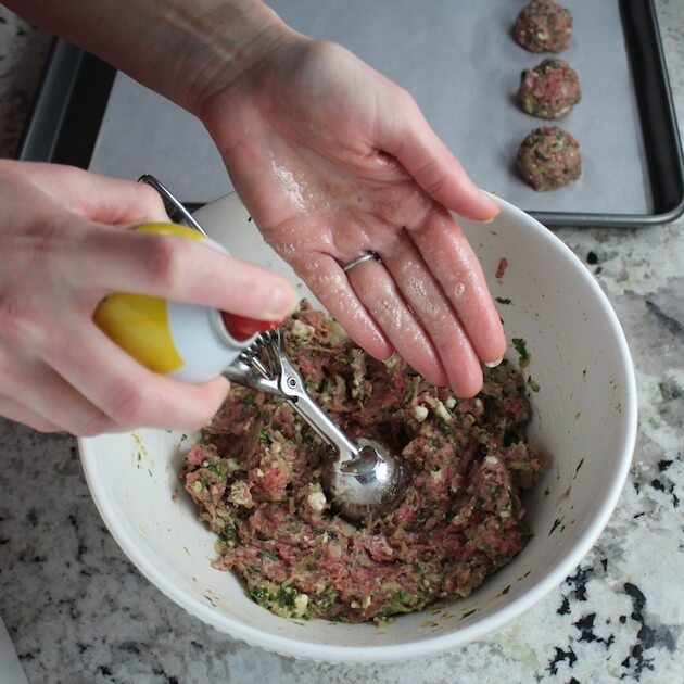 Spraying hands with oil to prepare meatballs for cooking