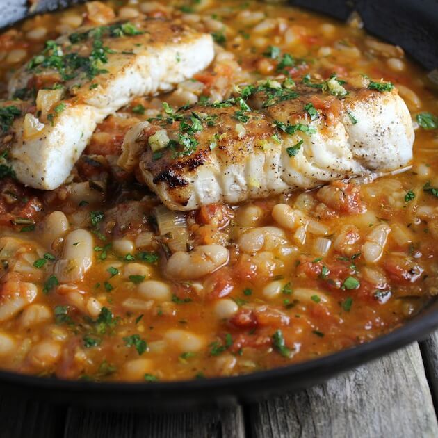 White fish in a saute pan with white beans and sauce