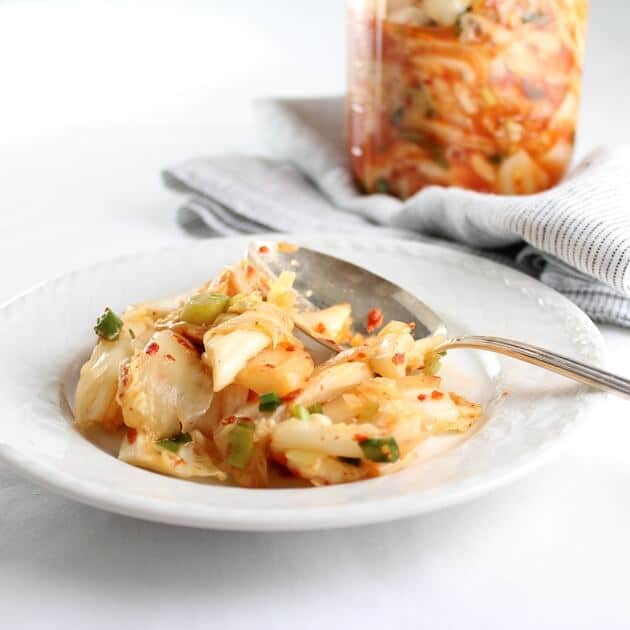 Homemade Kimchi in a bowl with a full mason jar of kimchi in  background