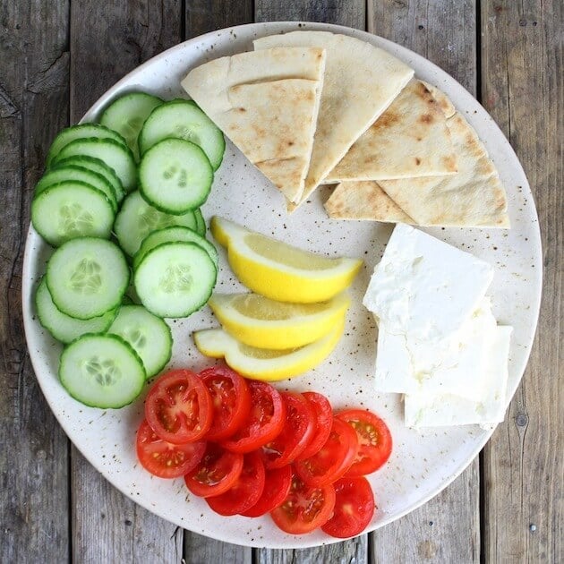 Platter of cucumbers, tomatoes, feta cheese, lemons and pitas for a Greek meal 