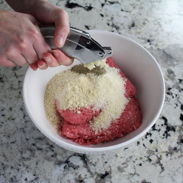 Mincing garlic into mixing bowl of italian meatball ingredients