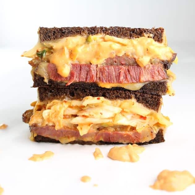 Two stacked halves of a reuben sandwich thick corned beef on pumpernickel bread