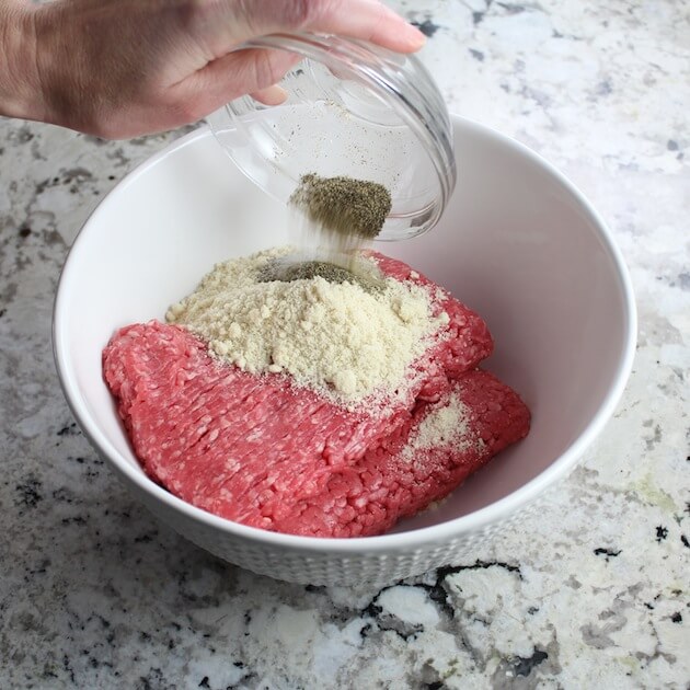 Adding salt and pepper to ground beef in mixing bowl