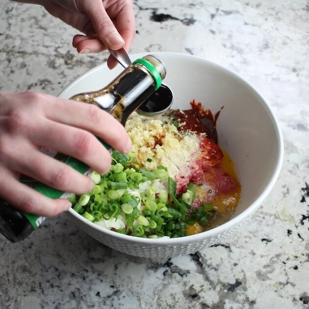 Adding soy sauce to bowl of ingredients.