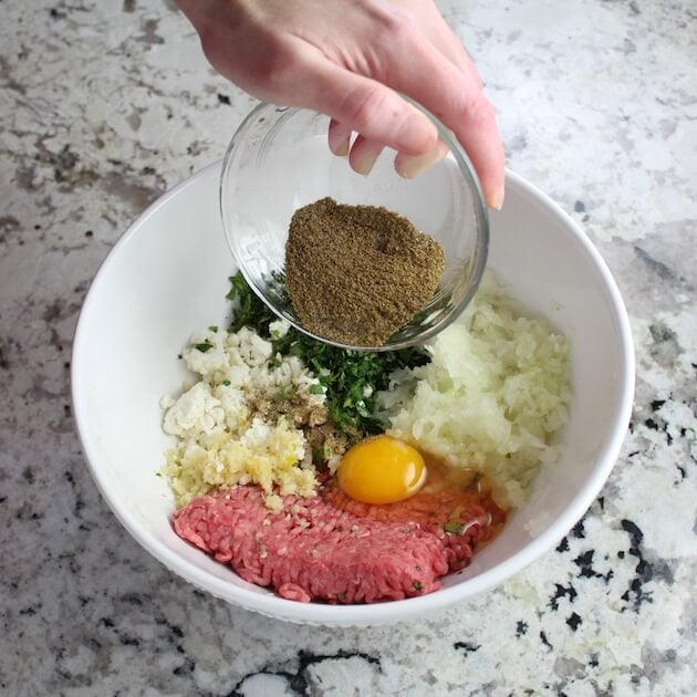 Adding spices to lamb meatball ingredients in large mixing bowl